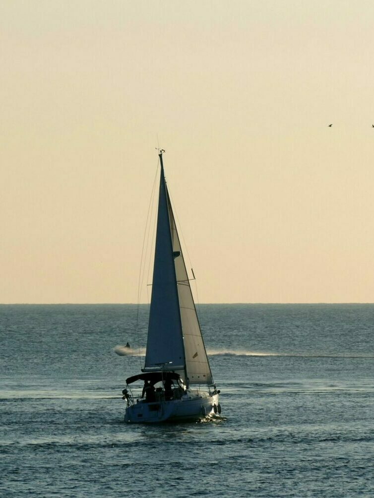 A serene sailboat glides on a calm sea at sunset, offering a peaceful maritime escape.